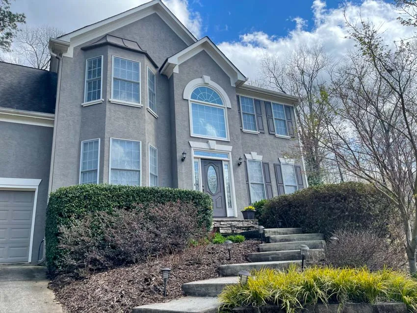 Gray stucco home with new windows above a landscaped front yard